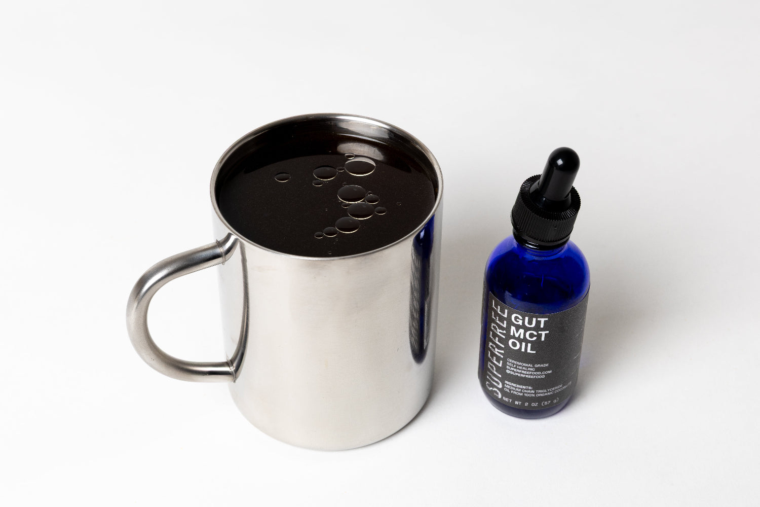 Stainless steel mug with coffee and a bottle of GUT MCT oil on a white background