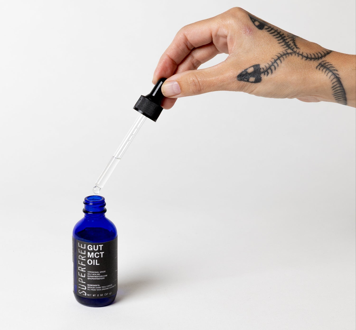 Hand holding a dropper over a blue bottle labeled 'GUT MCT' on a white background